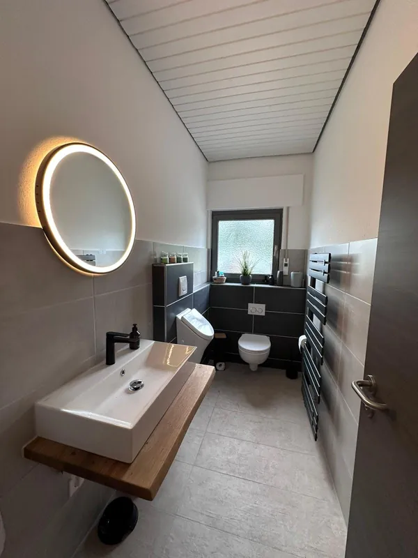 Renoviertes Badezimmer mit Waschtisch und beleuchtetem Spiegel