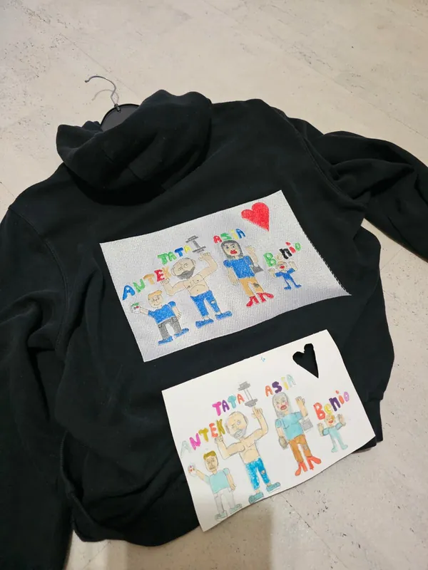 Kinderzeichnung und ihre Umsetzung als Stickerei auf einem schwarzen Hoodie